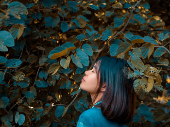 Side view of young woman standing with eyes closed by plants