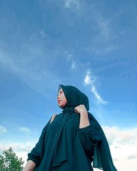 Low angle view of woman standing against blue sky