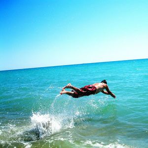 Man jumping in sea against clear sky