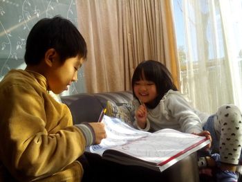 Siblings looking picture book while sitting on sofa at home
