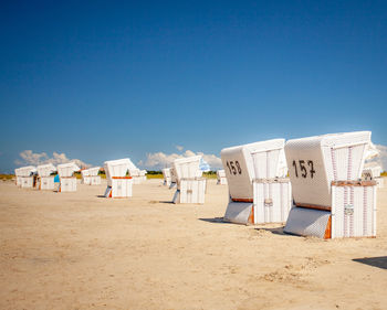 Hooded beach chairs on sand against clear blue sky