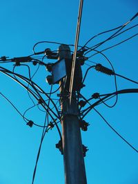 Low angle view of electricity pylon against clear blue sky