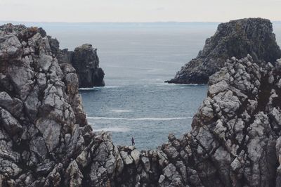 Scenic view of person standing on rock formation by the sea