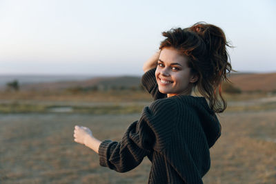 Young woman looking away while standing against sky