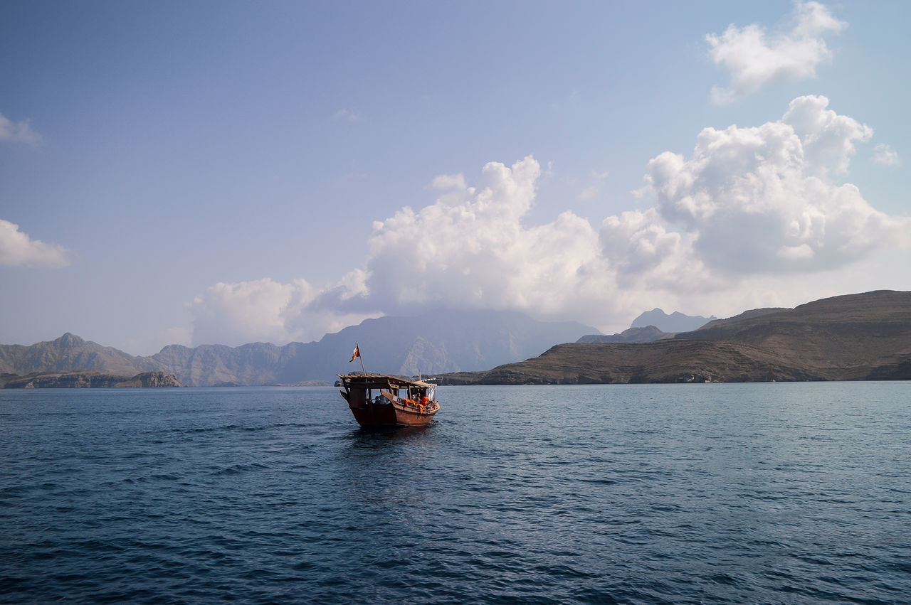 BOAT SAILING ON SEA AGAINST MOUNTAIN