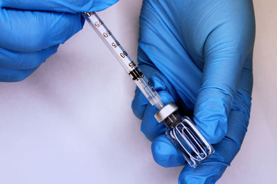 Hands in blue medical gloves close-up drawing up a vaccine from a vial into a syringe. 