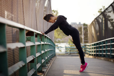 Determined female jogger stretching by railing on footpath