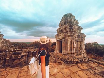 Rear view of man standing at historical building against cloudy sky