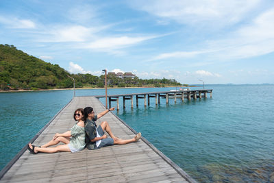 Portrait of couple sitting back to back on pier over sea