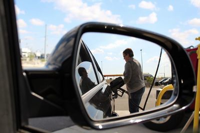 Reflection of woman refueling car on side-view mirror