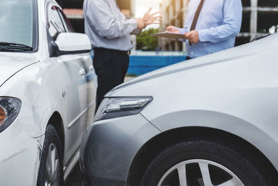 Midsection of insurance agent holding clipboard while client standing outdoors