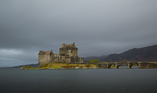 Built structure by lake against cloudy sky