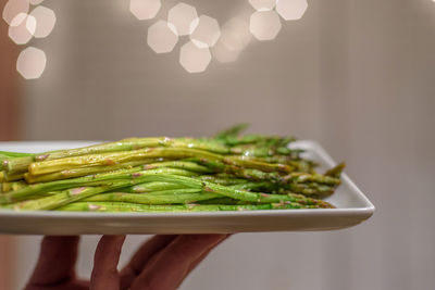 Closeup of hand holding up a plate of fresh steamed asparagus