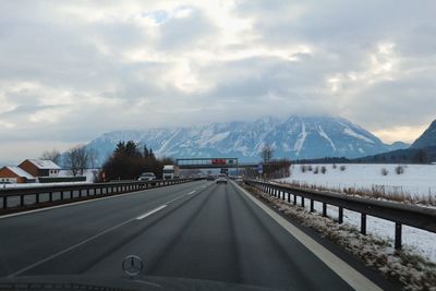 Road by mountains against sky during winter