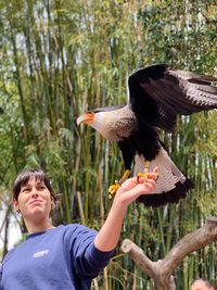 Portrait of man holding bird flying against trees