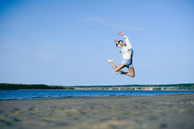 Woman jumping at beach against blue sky