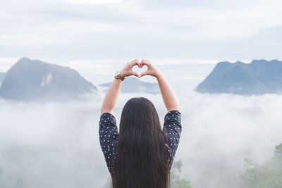 Rear view of woman making heart shape while looking at mountains