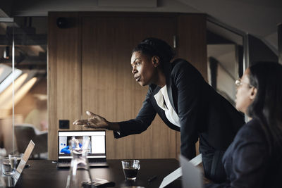 Side view of businesswoman gesturing during meeting while leaning at desk in office