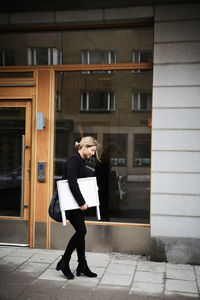 Full length of real estate agent walking with blank signboard on sidewalk in city