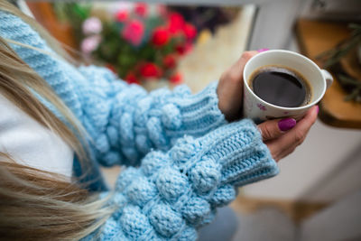 A woman warms her frozen hands against a mug of hot coffee.