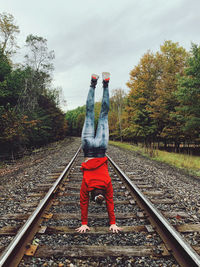 Rear view of girl doing hand stand by railroad tracks against sky
