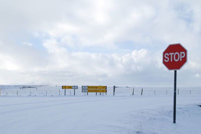 Road sign on snow covered landscape against sky