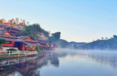 Houses by lake and buildings against clear sky