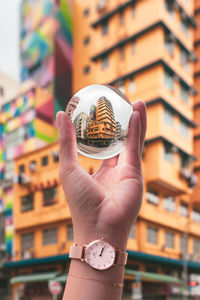 Close-up of hand holding clock against blurred buildings