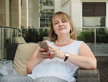 Portrait of mature woman using phone while sitting on chair