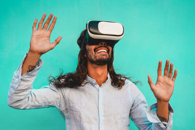 Smiling man looking through virtual reality simulator against blue background