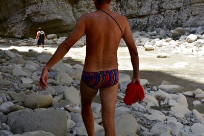 Midsection of shirtless man walking at riverbank