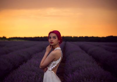 Side view of female model looking up while standing at lavender field during sunset