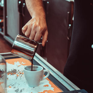 Midsection of man holding coffee cup on table