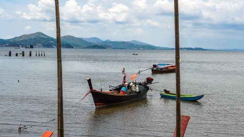 Boats moored in sea against cloudy sky