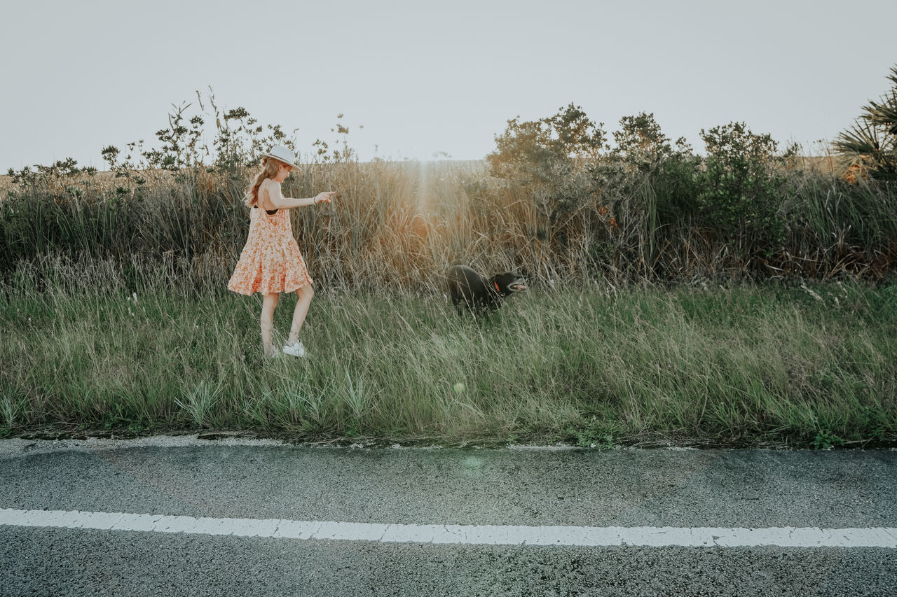 WOMAN STANDING BY ROAD AGAINST SKY