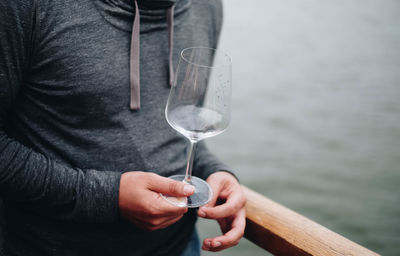 Midsection of man holding wineglass while standing by railing