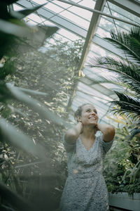 Smiling young woman standing against plants