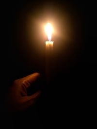 Close-up of hand holding lit candle in the dark