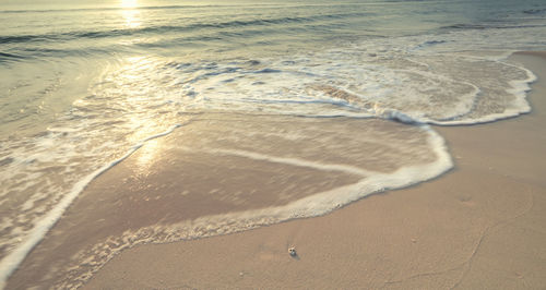 Long exposure shot sandy beach and the sea wave white bubbles with the sunrise background 