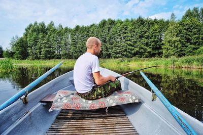 Man sitting by lake against sky