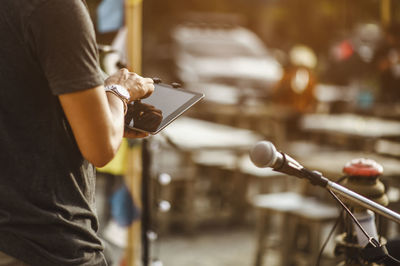 Midsection of man holding digital tablet standing by microphone