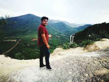 Full length of young man standing on rock against sky