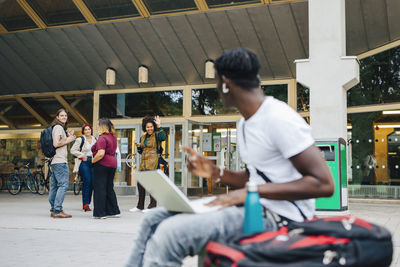 Male student looking at friends while using laptop in campus