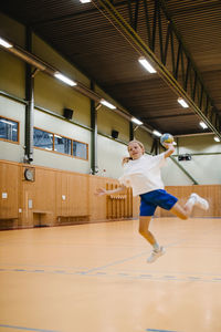 Girl jumping while throwing handball in sports court