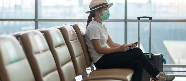 Woman wearing mask with luggage sitting in airport