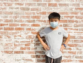 Portrait of boy in facemask standing against brick wall
