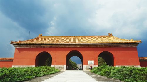 Road leading towards arched building against cloudy sky