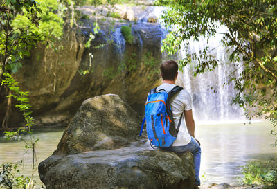 Rear view of man sitting on rock by lake