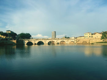 Bridge over river by buildings against sky