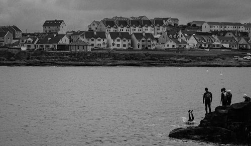 People on rocks by sea against sky